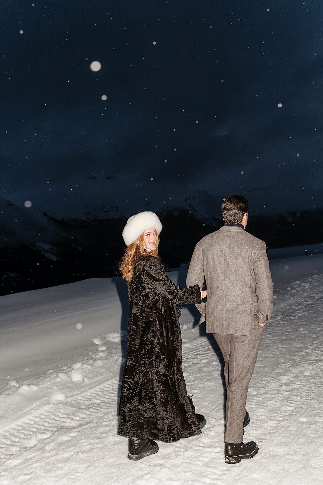 Bride and groom under the snow at the welcome dinner of old world winter wedding in Saint Moritz